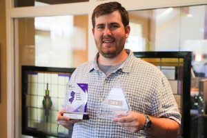 man posing with two awards